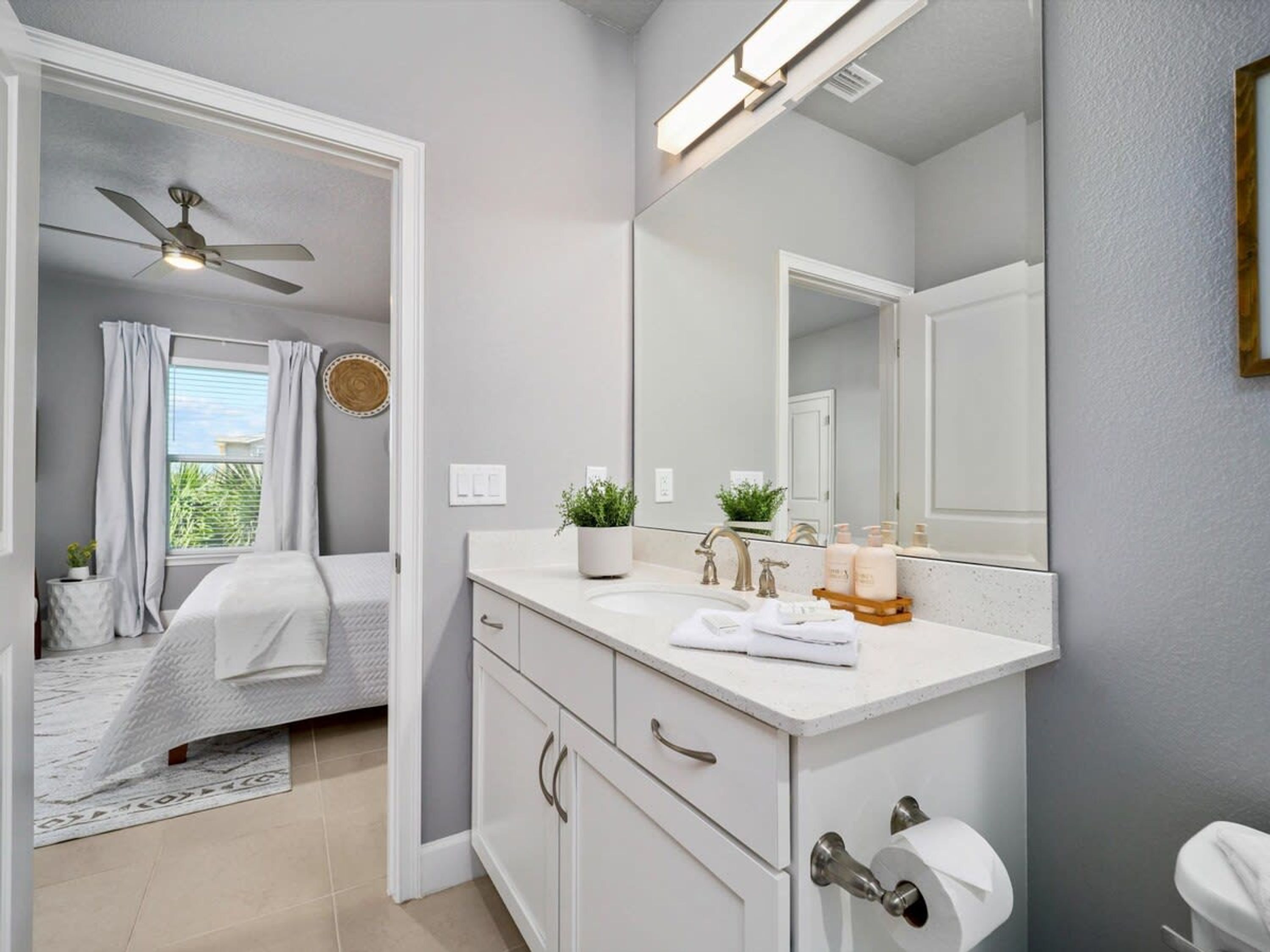 A modern bathroom with a large mirror, white vanity, and a ceiling fan.