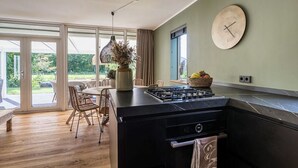 Een moderne keuken met een groot kookeiland, een zithoek met rieten stoelen en uitzicht op de tuin via grote schuifdeuren.