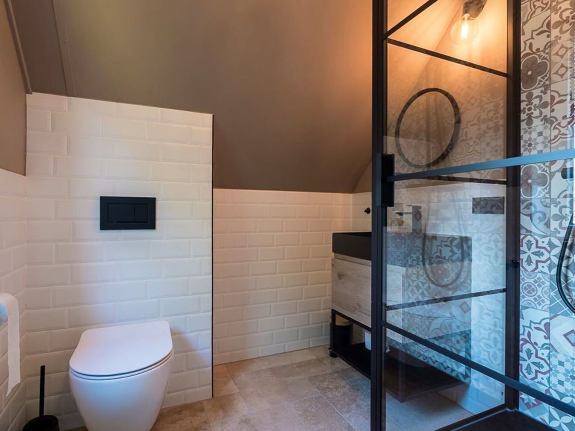 Une salle de bain avec des toilettes blanches, une douche en verre et des carreaux décorés.