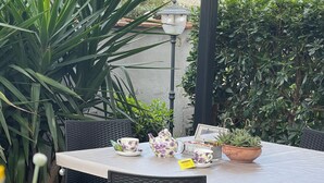 An outdoor patio with a table set for tea, surrounded by wicker chairs, and various potted plants. - LUCCA MIRA (Lucca)