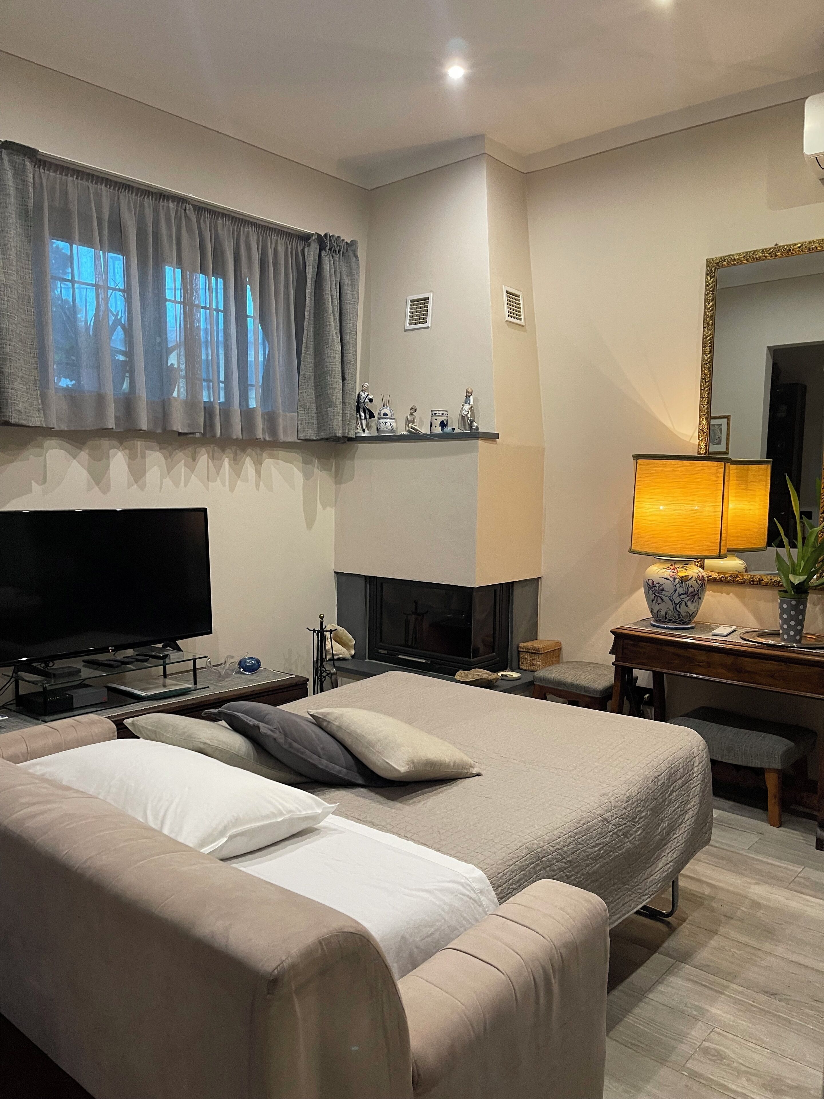 A modern hotel room with a large bed, a flat-screen TV, a fireplace, and a desk with a lamp.