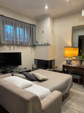 A modern hotel room with a large bed, a flat-screen TV, a fireplace, and a desk with a lamp.