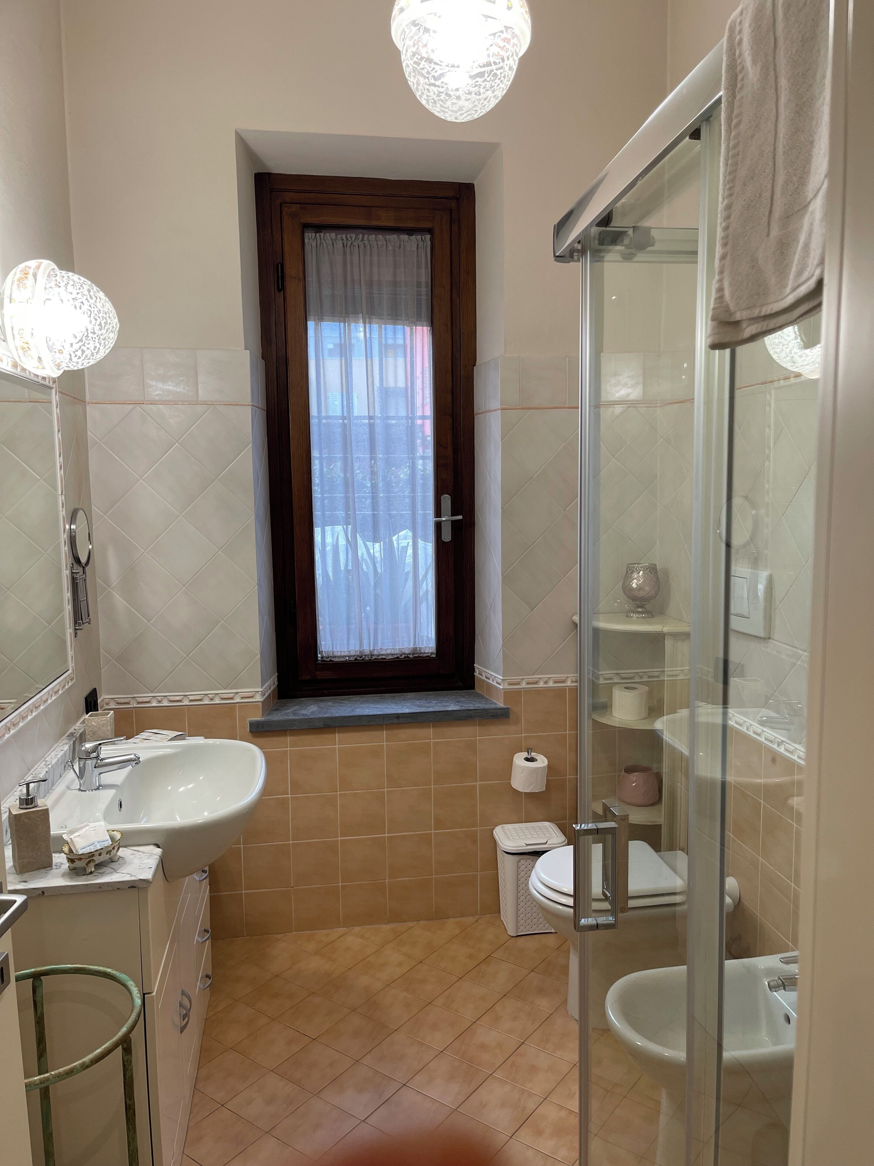 A bathroom with a sink, toilet, and bidet, a window with curtains, and a shower area.