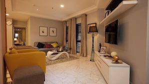 Een moderne woonkamer met een bank, fauteuils, een salontafel en een aan de muur bevestigde televisie.
