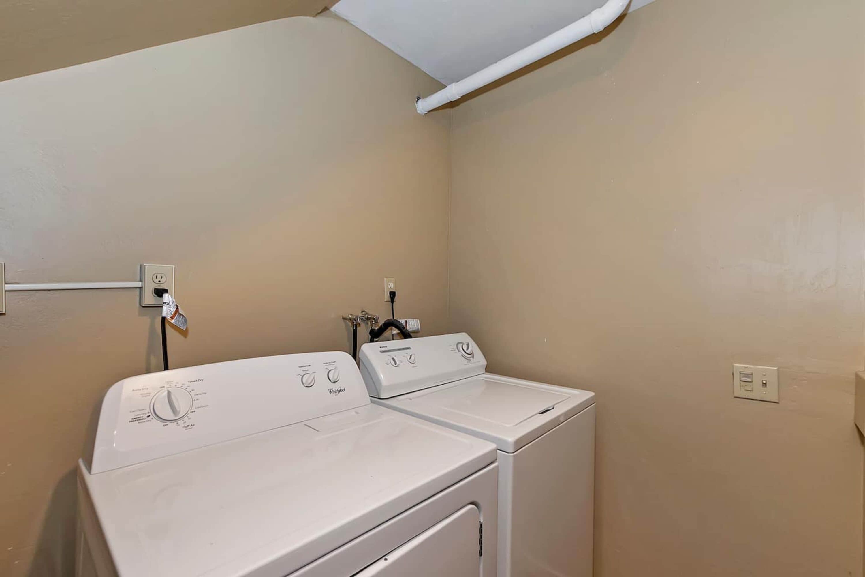 A laundry room with two white washers and dryers, beige walls, and a ceiling vent.