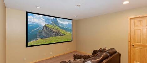A home theater room with a large flat-screen TV mounted on the wall, a brown leather recliner, and a wooden door.