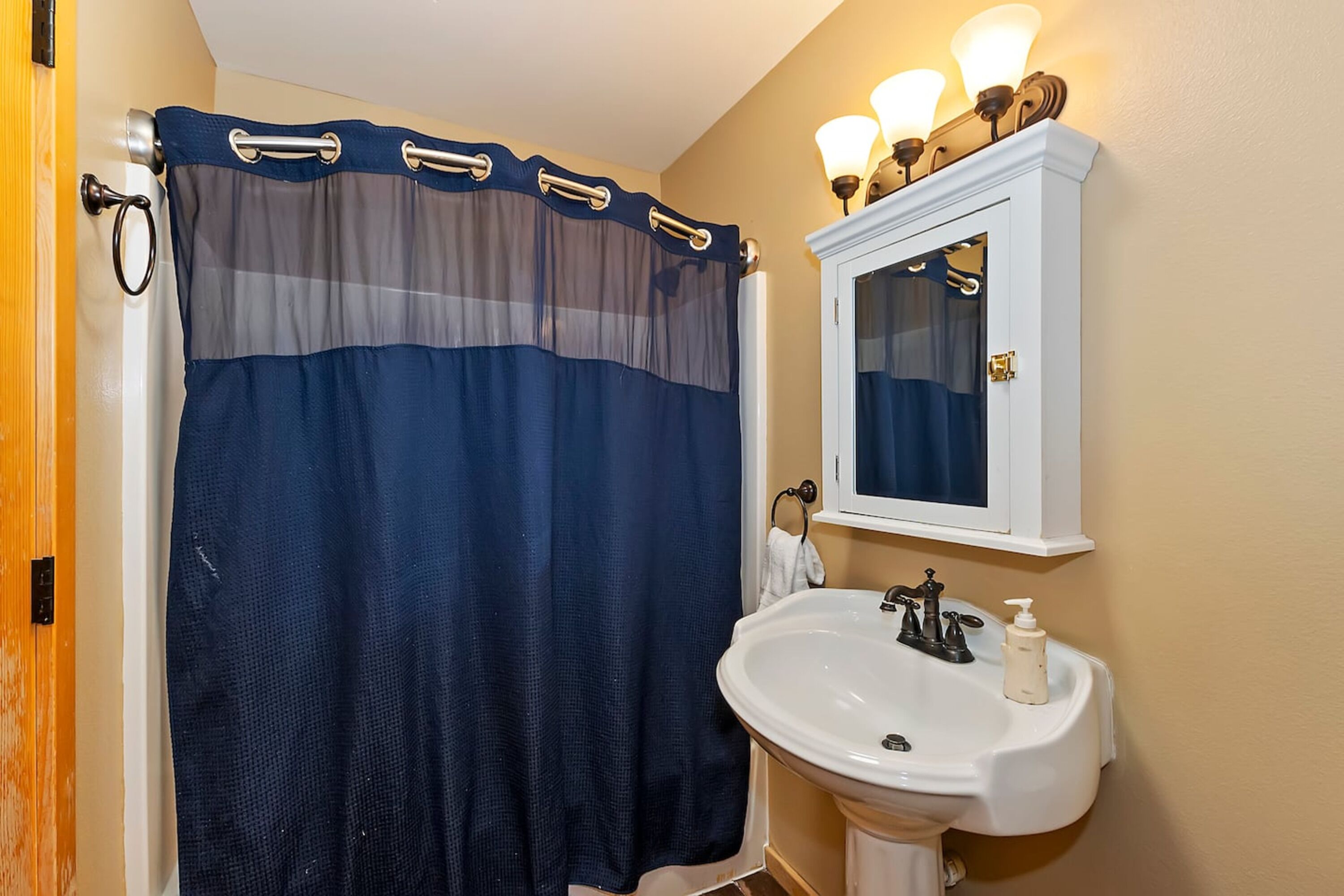 A bathroom with a dark blue shower curtain, a white sink with a mirror above it, and a wall-mounted light fixture.