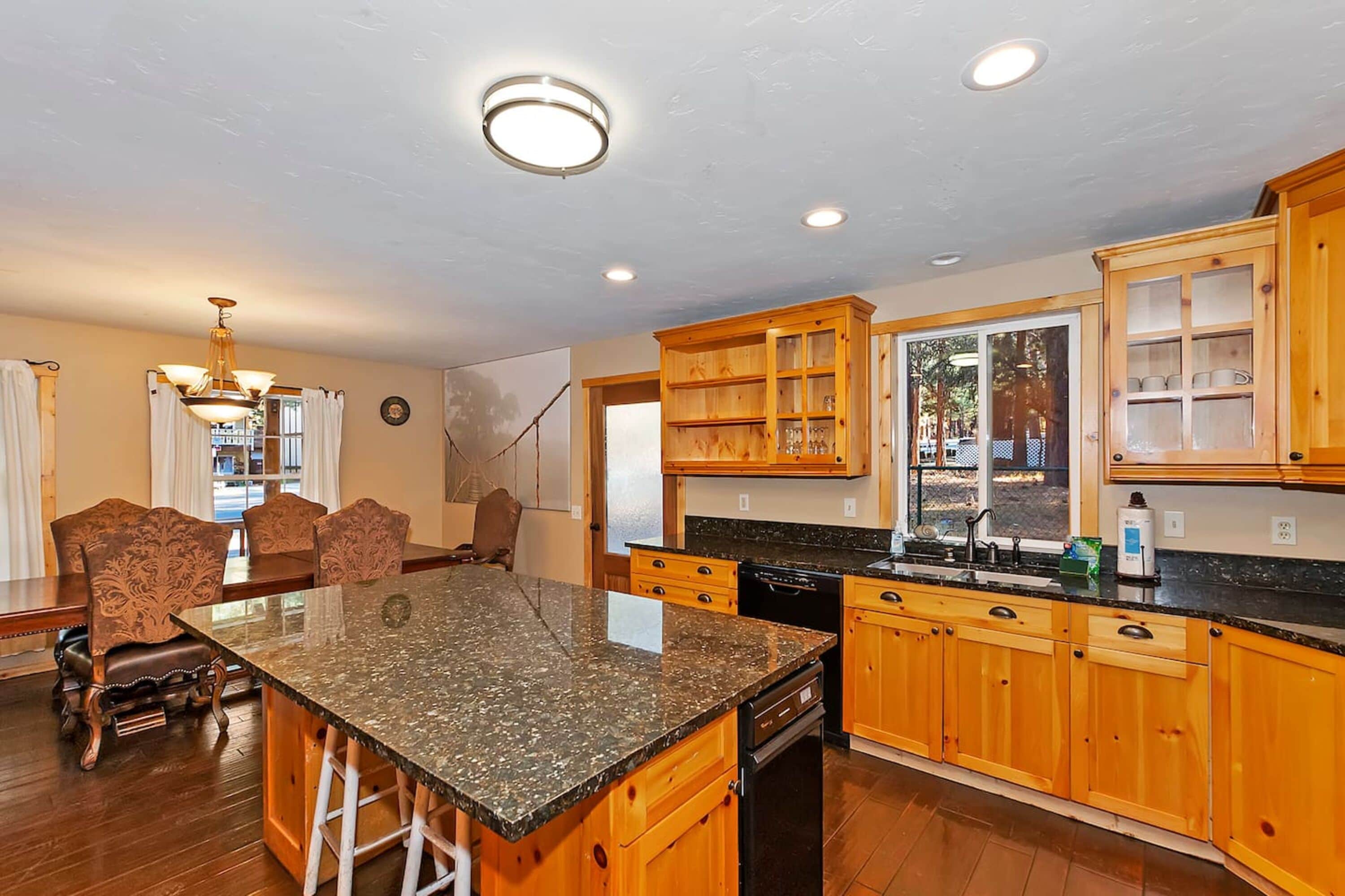 A kitchen with wooden cabinets, a granite countertop, and a dining area with chairs.