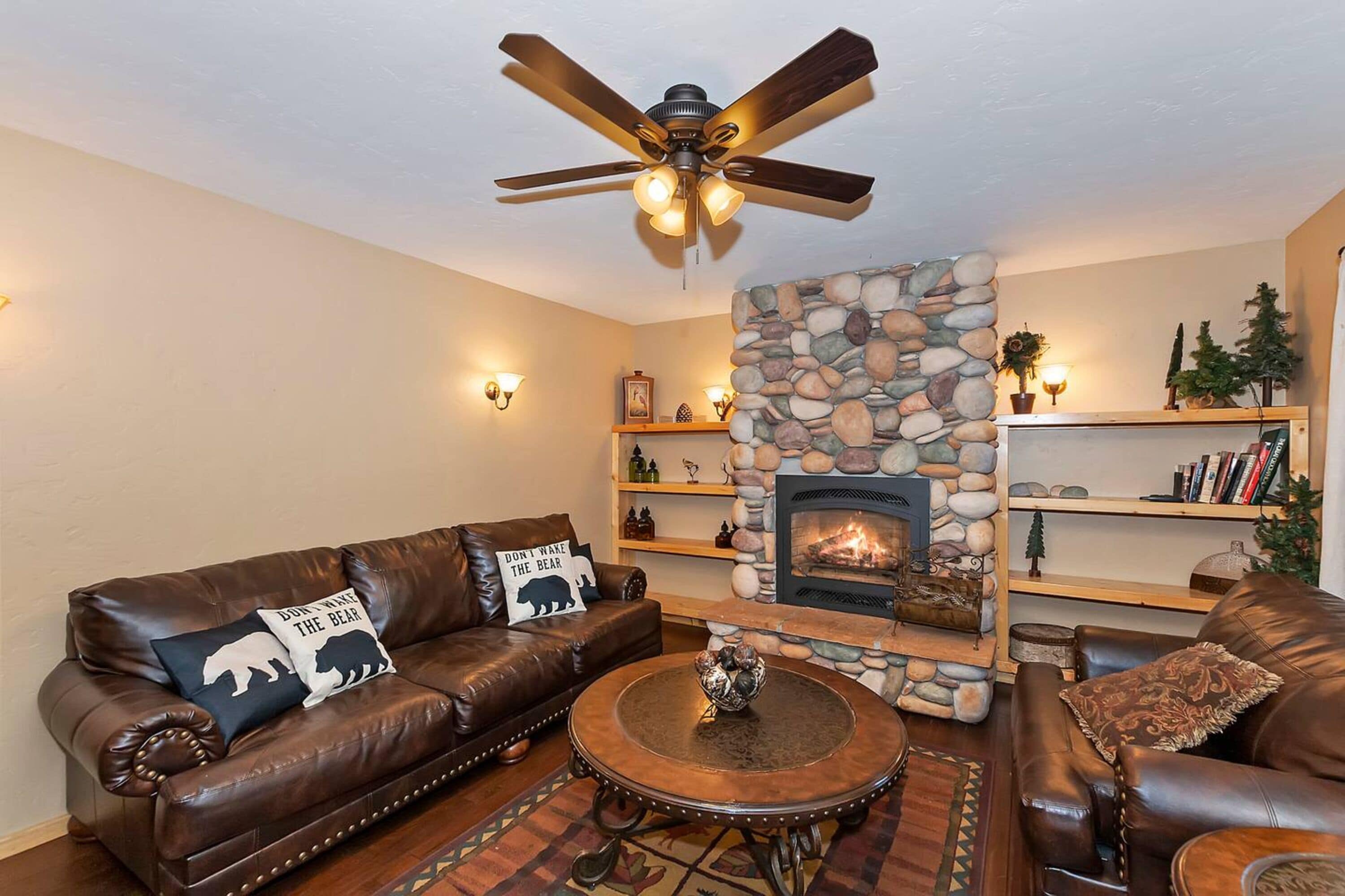 Ein gemütliches Wohnzimmer mit Kamin aus Stein, Ledersofas und Deckenventilator.