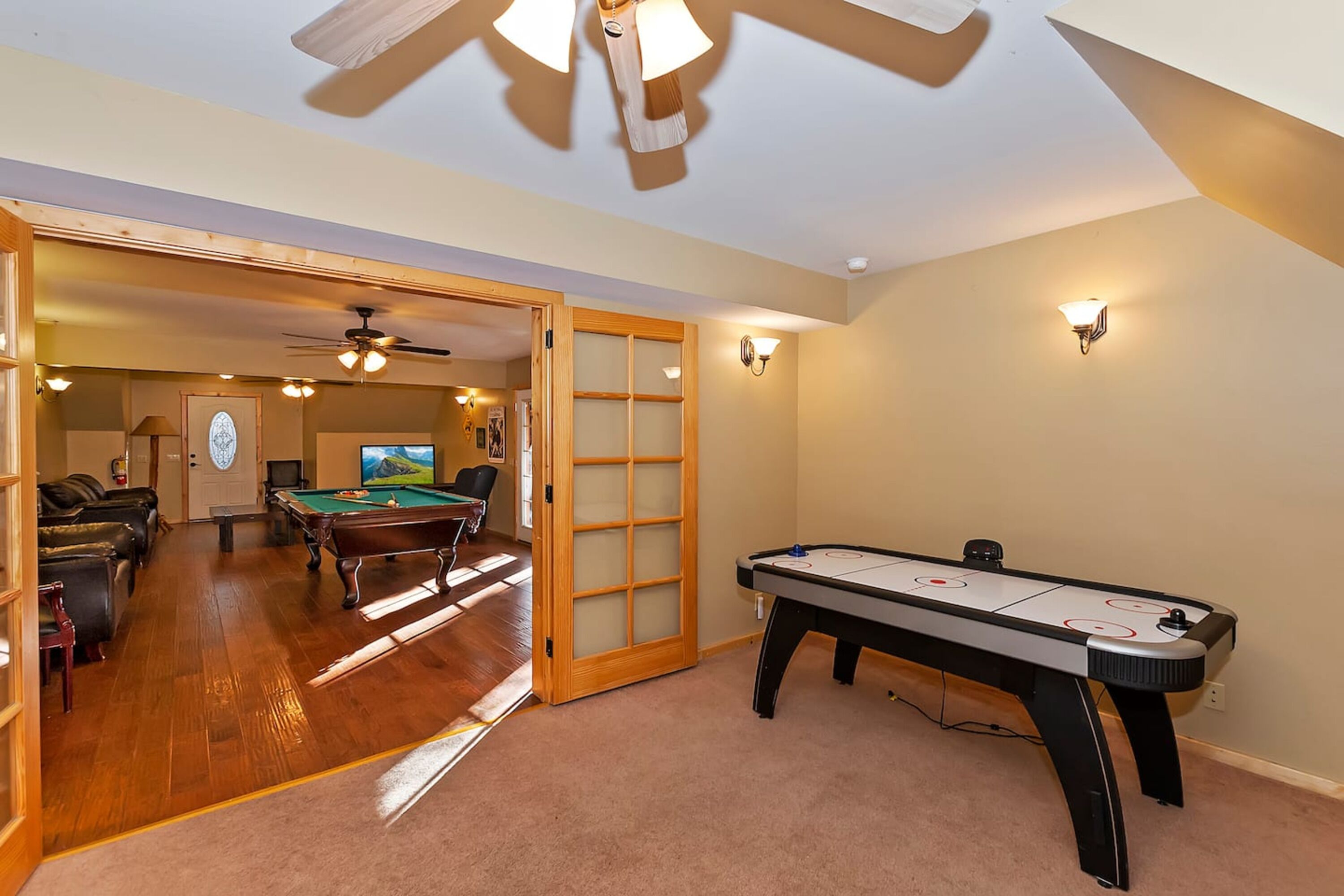 Ein Zimmer mit Billardtisch, Deckenventilator und einer Tür zu einem weiteren Zimmer mit Billardtisch und Snookertisch.