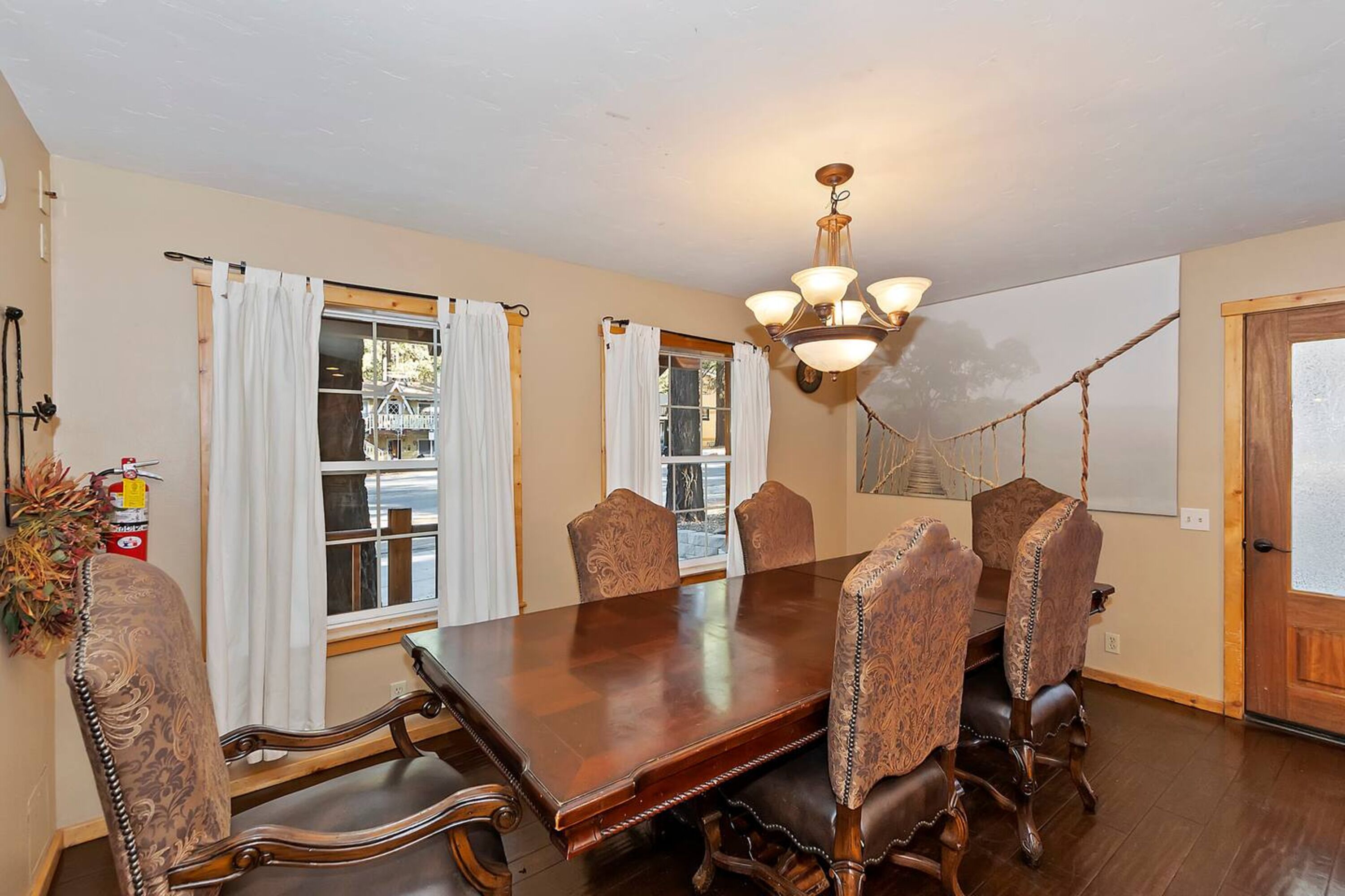 A dining room with a large wooden table, six upholstered chairs, and a chandelier.
