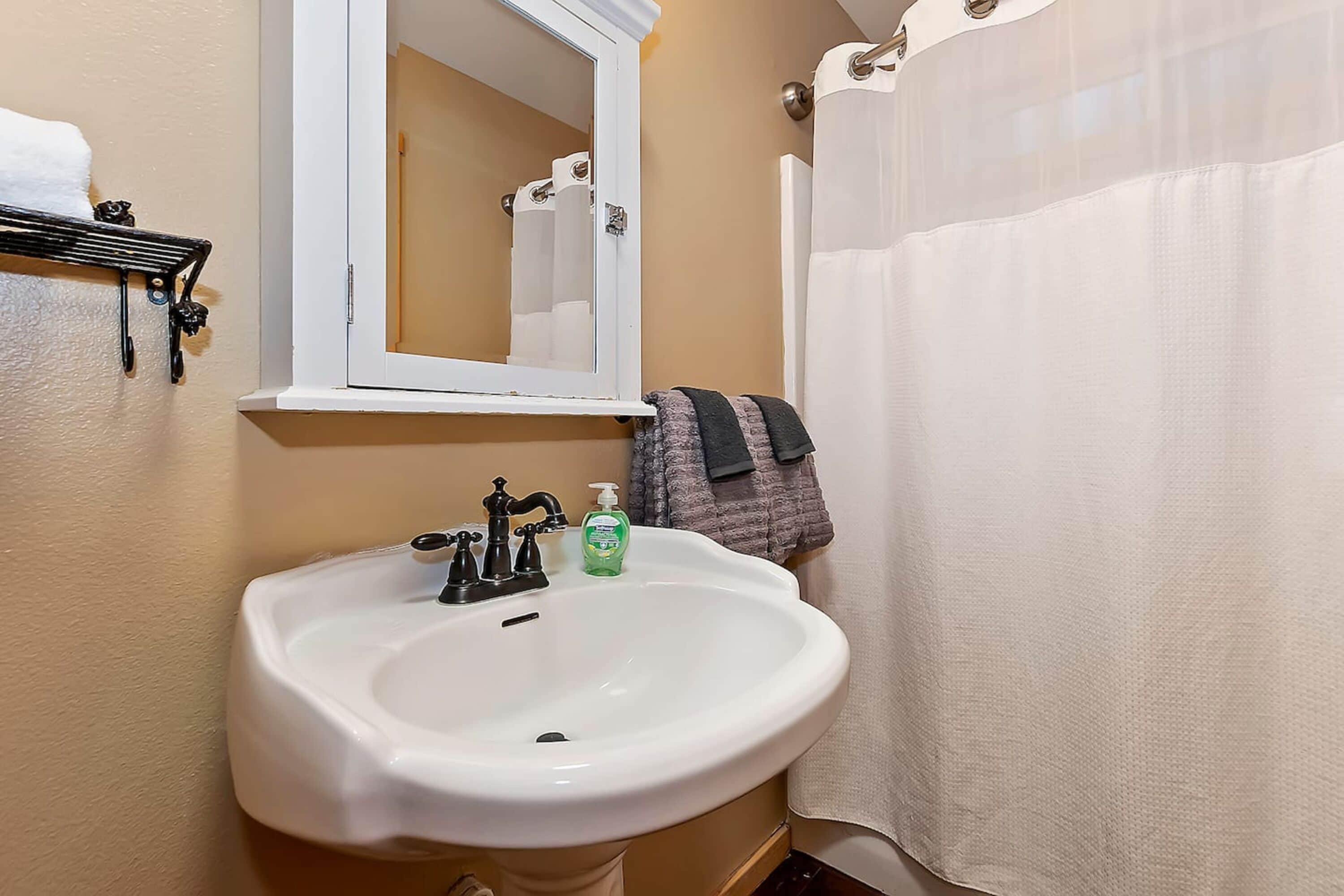 A bathroom with a white sink, a mirror, a towel rack, and a shower curtain.