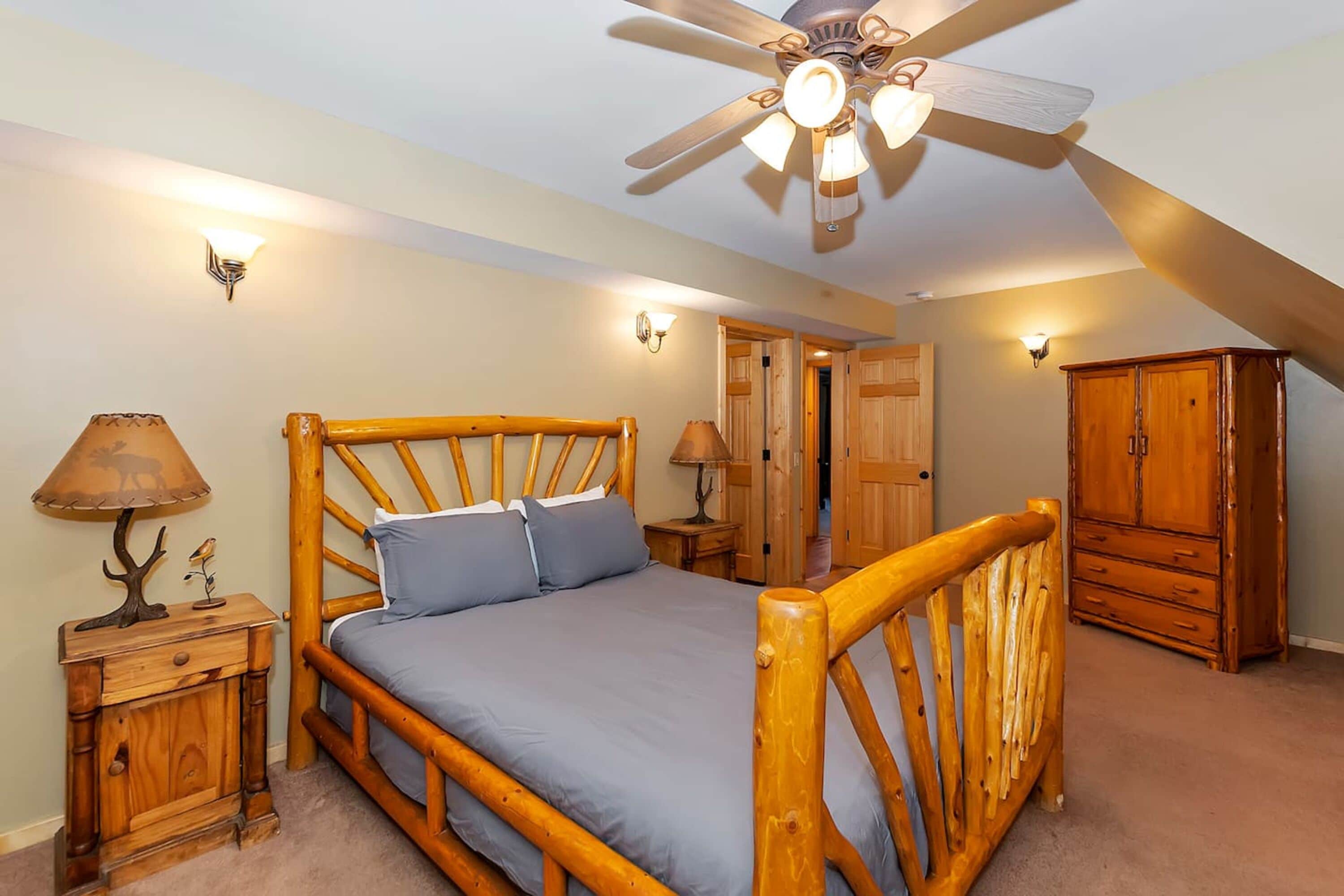 Une chambre avec un lit en bois, un ventilateur de plafond et une armoire.