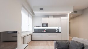 A modern kitchen with white cabinets, a microwave, and a sink. There is a gray sofa in the living area. - De Amicis 25 - Nel cuore di Milano (Milan)