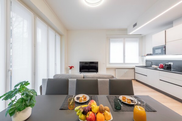 Una cocina moderna con zona de comedor, un sofá y televisión al fondo.