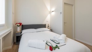 A neatly made bed with white linens, a vase with red flowers, and a rolled towel on the bed. - De Amicis 25 - Nel cuore di Milano (Milan)
