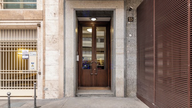 A building entrance with a wooden door, a metal gate, and a closed shutter on the right. - De Amicis 25 - Nel cuore di Milano (Milan)