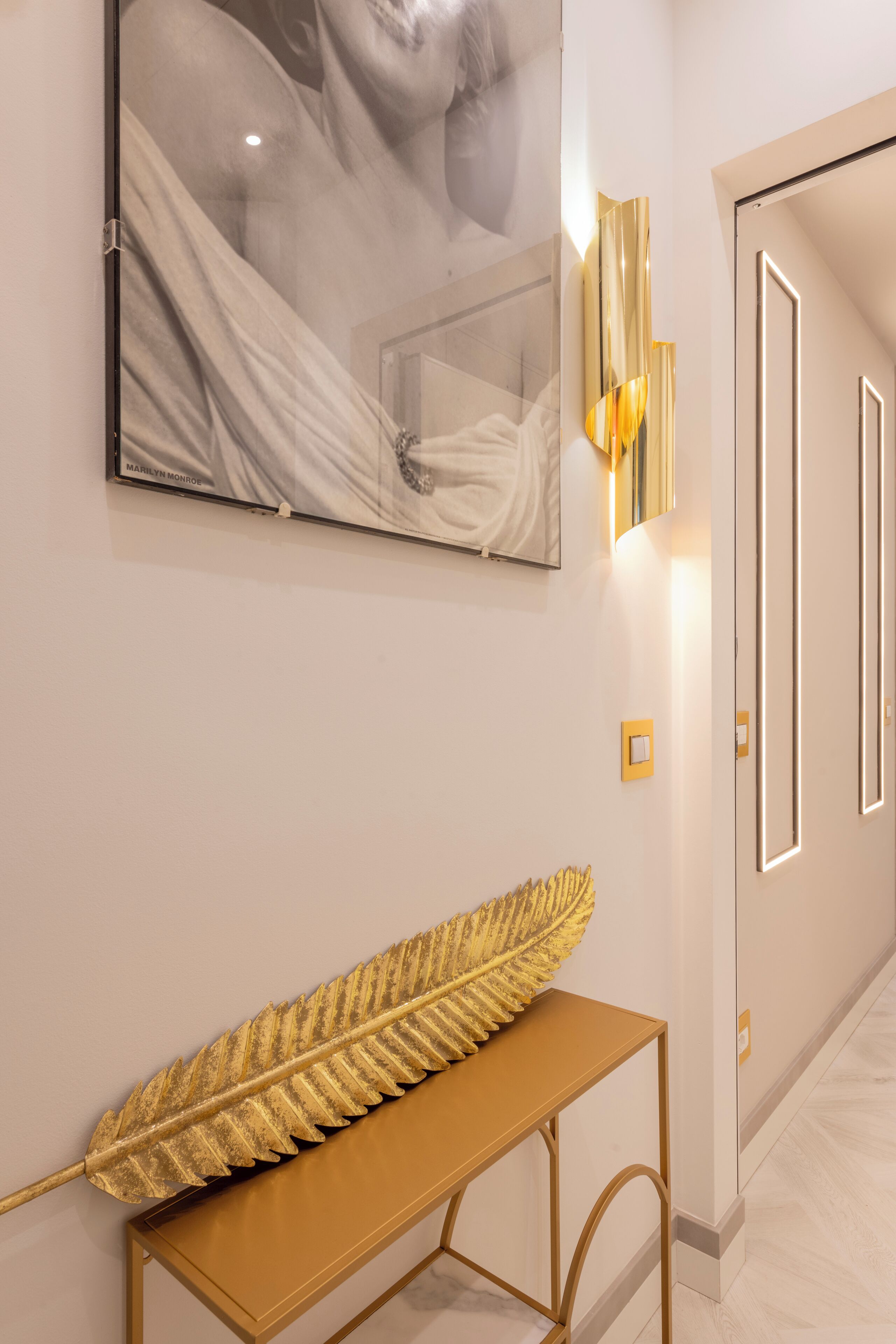 A hallway with a large framed artwork, a golden leaf decoration on a table, and modern wall sconces.