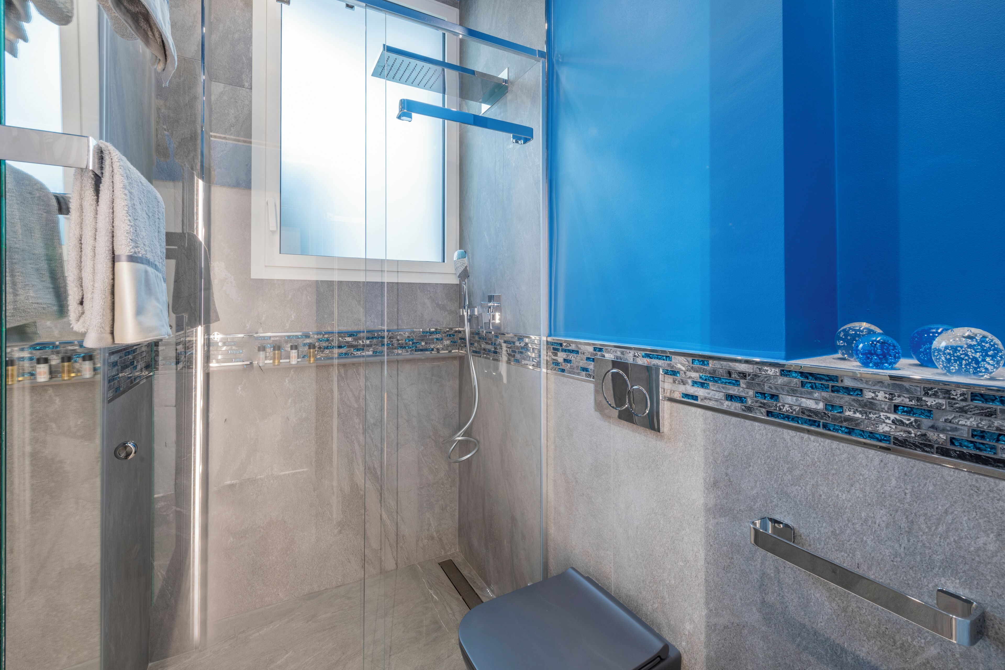 A modern bathroom with a glass shower enclosure, a small bench, and a vanity with a blue mosaic backsplash.