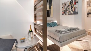 Habitación de hotel moderna con una cama, una mesita con una botella de champán y copas, y arte abstracto en las paredes.