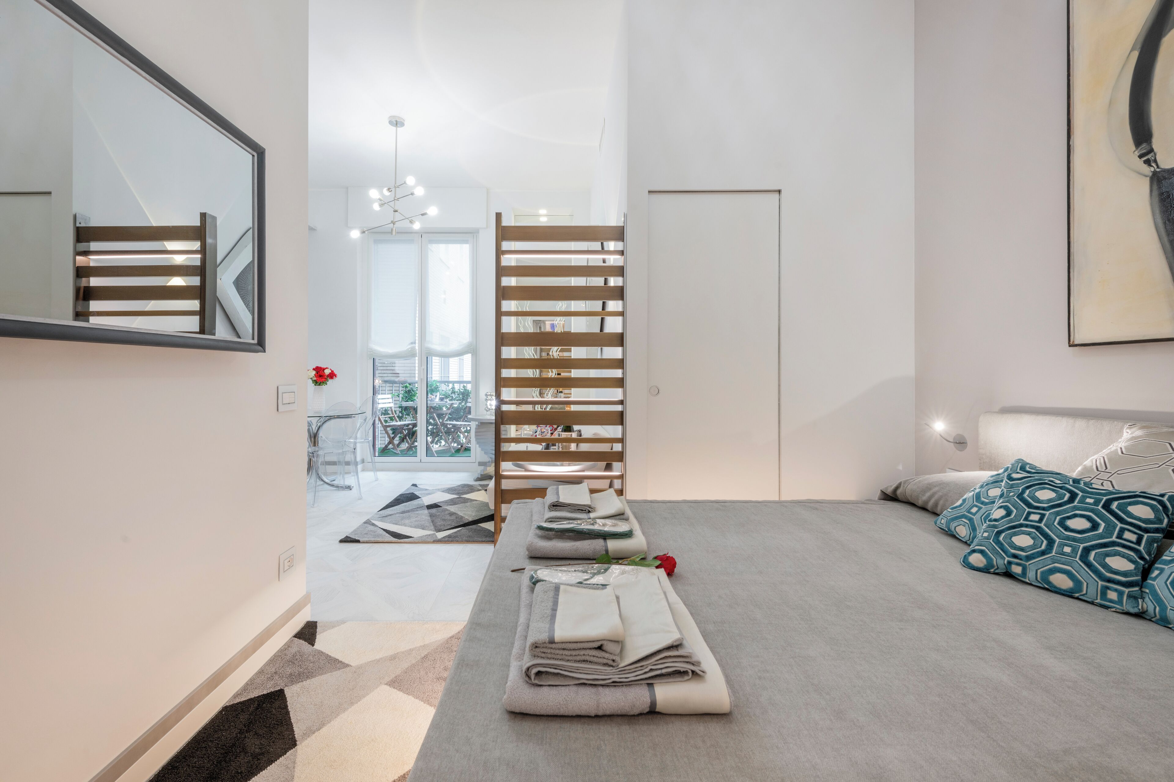 Een moderne slaapkamer met een bed, een bankje met handdoeken, een houten lattenwand en een grote spiegel.