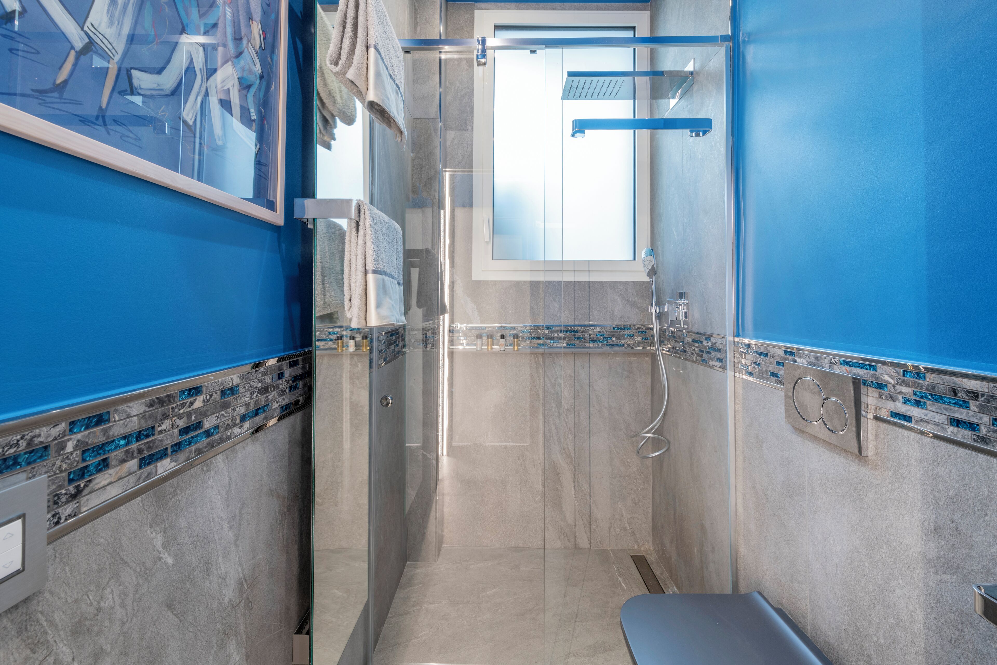 A modern bathroom with a glass shower enclosure, a sink with a mirror, and a blue accent wall.
