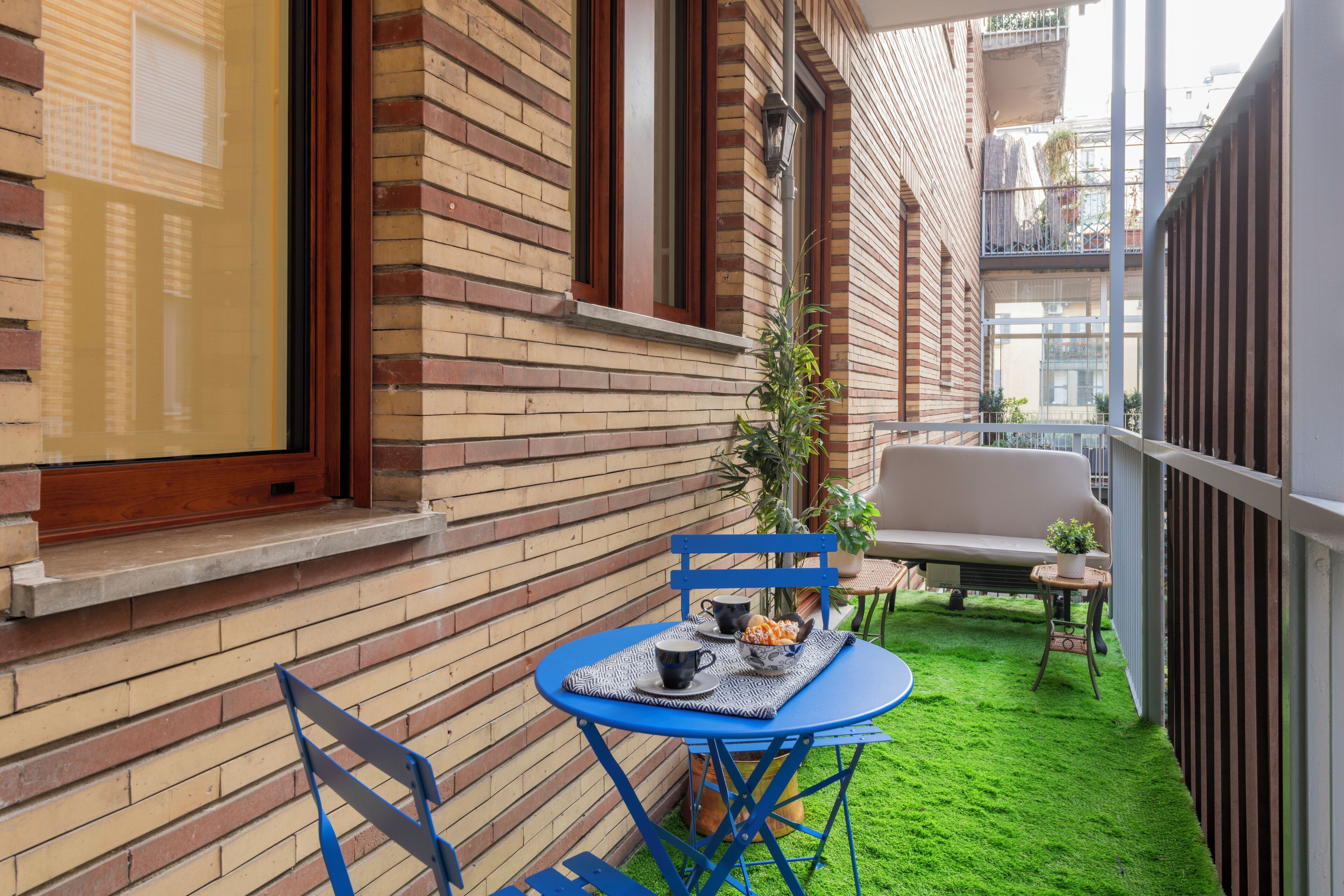 Une petite terrasse extérieure avec une table et des chaises bleues, une plante en pot et un canapé blanc.