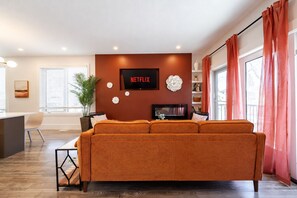 Un salon avec un grand canapé orange, un téléviseur à écran plat fixé au mur et une plante en pot.