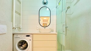 A modern bathroom with a washing machine, a sink with a mirror, and a glass-enclosed shower. - Unique by Grand Apartments (Sopot)