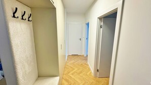 A hallway with a wooden floor, white walls, and a white door at the end. - Unique by Grand Apartments (Sopot)