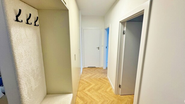 A hallway with a wooden floor, white walls, and a white door at the end. - Unique by Grand Apartments (Sopot)
