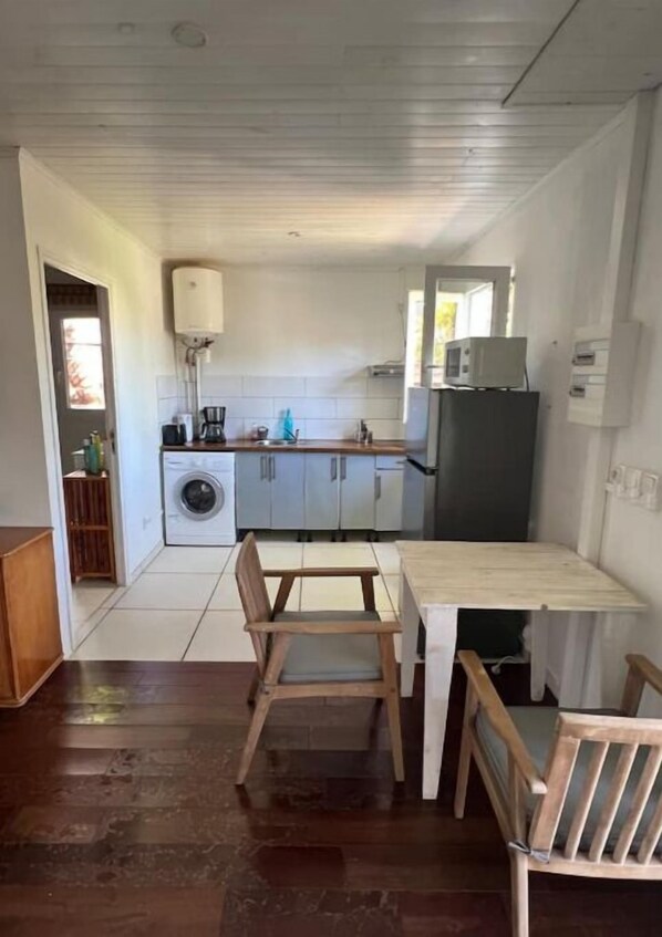 A compact kitchen with a dining table and chairs, a washing machine, and a refrigerator. - TI KAZ with SPA and nearby lagoon (Saint-Paul)