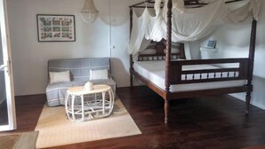 A bedroom with a four-poster bed, a sofa, a small table, and a hanging light fixture. - TI KAZ with SPA and nearby lagoon (Saint-Paul)