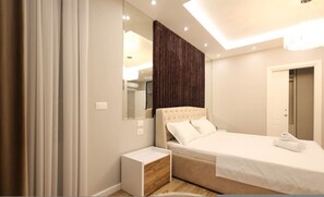 A modern bedroom with a bed, bedside table, and a mirror. - Grandstay Apartments 007 (Durrës)