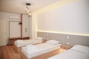 Une chambre d’hôtel avec trois lits simples, une armoire et un luminaire au plafond.