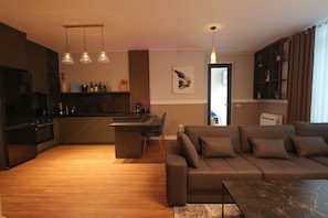 A modern living room with a sofa, a coffee table, and a kitchen area with a dining table and chairs. - Grandstay Apartments 001 (Durrës)