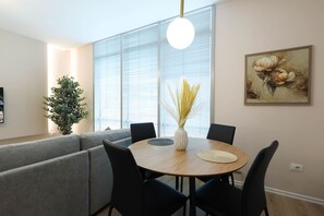 Un espace repas moderne avec une table ronde, des chaises noires, un canapé gris, une plante en pot et un tableau au mur.