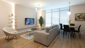 Una sala de estar moderna con un sofá, una mesa de comedor con sillas, un televisor y una planta en maceta.