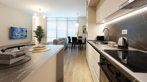 Una cocina moderna con estufa integrada, un comedor con mesa y sillas, y un ventanal que ofrece vistas a la ciudad.