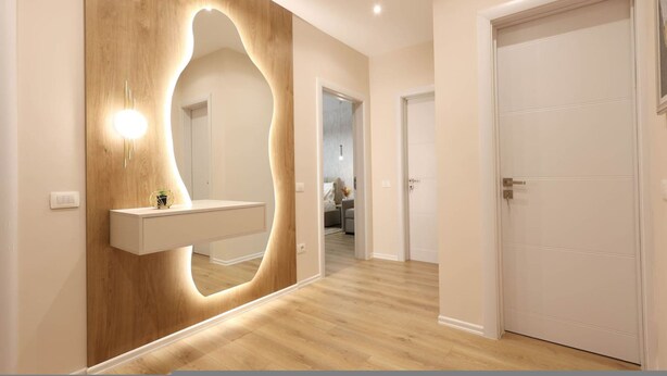 Un pasillo con un revestimiento de madera, una puerta blanca y un espejo con iluminación integrada.