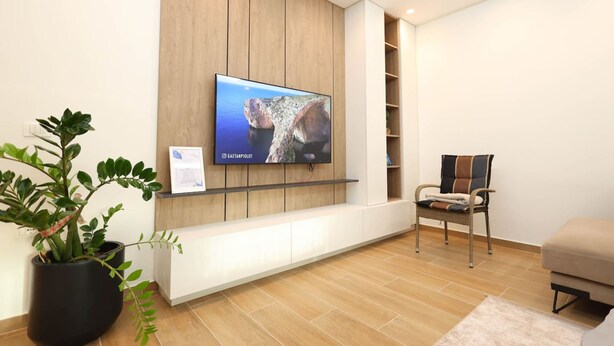 Ein modernes Wohnzimmer mit einem Wand-Fernseher, einer Holzpaneelwand, einer Topfpflanze, einem gepolsterten Sessel und einem Sofa.