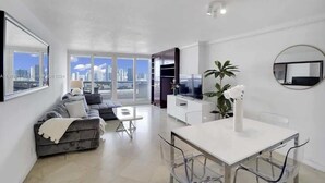 A modern living room with a sofa, a dining table, and a TV. - High Rise | Premium Amenities | BayView | StayCozy (Miami)