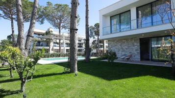 A modern two-story building with a stone facade, large windows, and a swimming pool in the background.