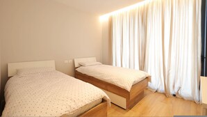 Une chambre avec deux lits, un plancher en bois et une grande fenêtre avec des rideaux.
