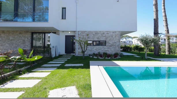 Une maison moderne à deux étages, dotée d’une piscine, d’un chemin en pierre et d’un petit jardin.