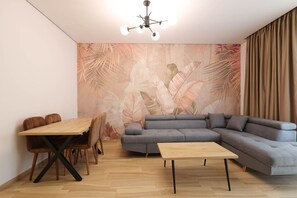 Ein modernes Wohnzimmer mit einem Ecksofa, einem Holzesstisch mit Stühlen und einer Wand mit Blättermustern.