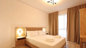 Een moderne hotelkamer met een groot bed, een houten hoofdbord, bedlampjes en uitzicht op het landschap door grote ramen.