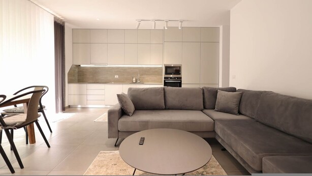 Un salon moderne avec un canapé d’angle gris, une table basse ronde et un coin repas comprenant une table et des chaises.