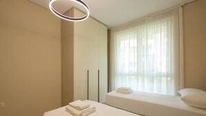 Ein Hotelzimmer mit zwei Betten, einem großen Fenster mit durchsichtigen Vorhängen und einer modernen Deckenleuchte.