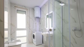 Un baño moderno con cabina de ducha de vidrio, lavadora integrada y lavamanos.